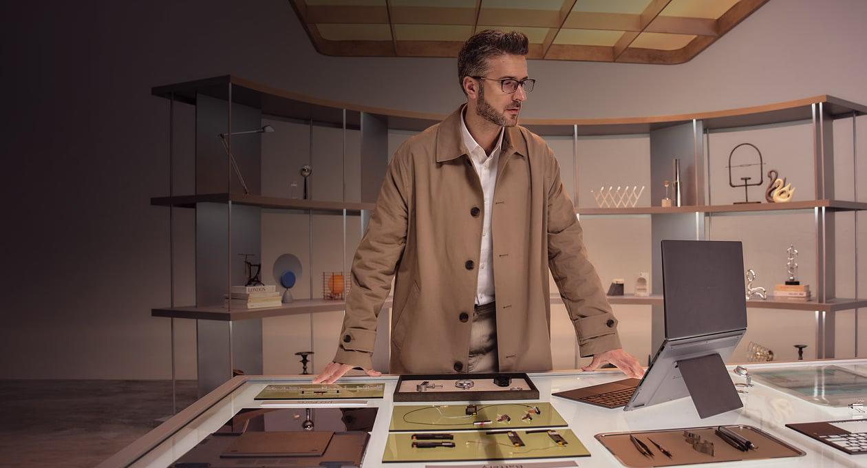 一名男子站在一张桌子后面，桌子上摆放着多个关键零件，前方则放着一台打开的 ASUS灵耀双屏笔记本电脑。