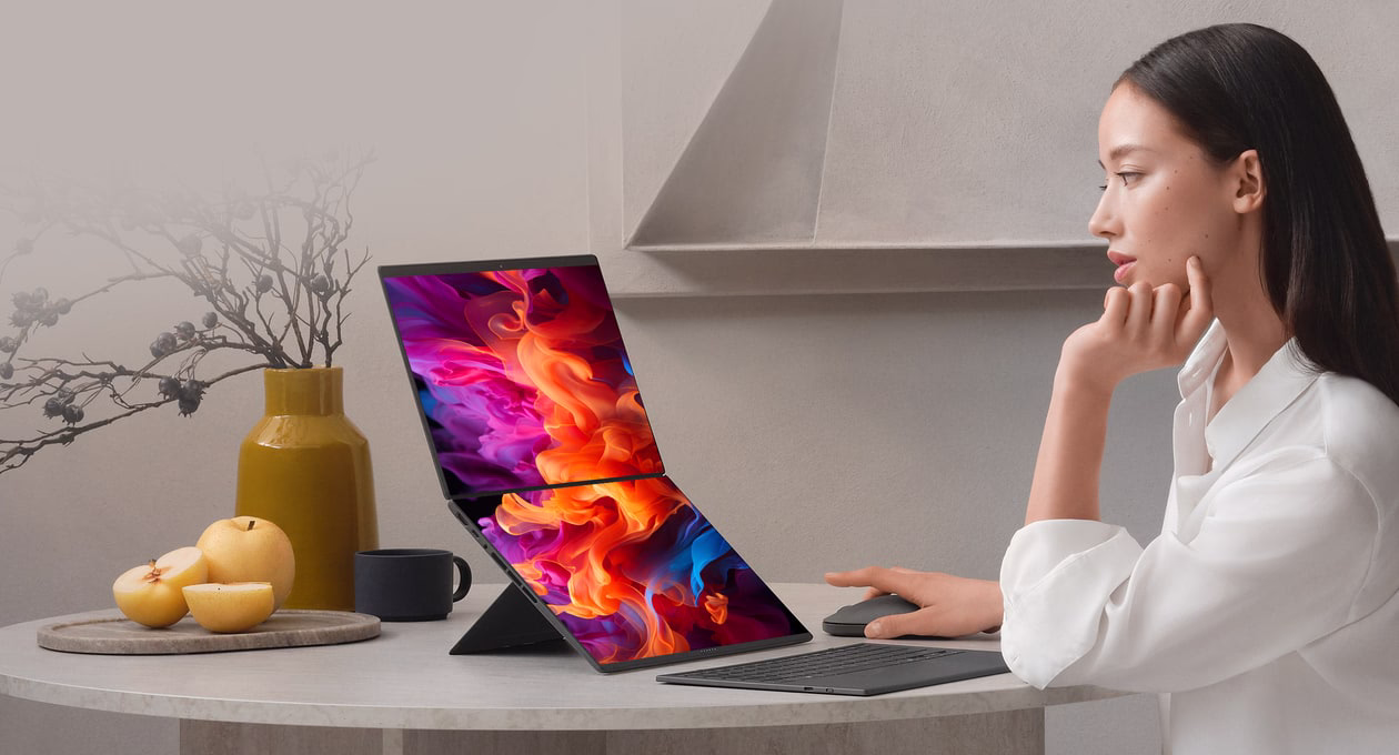 一位女士坐在圆桌旁，面前是一台 ASUS灵耀双屏笔记本电脑，屏幕上显示着生动的抽象图片。