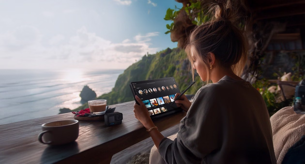 一位创作者坐在户外的木桌旁，使用触控笔操作触控屏幕笔记本，温暖的自然光照亮了屏幕。