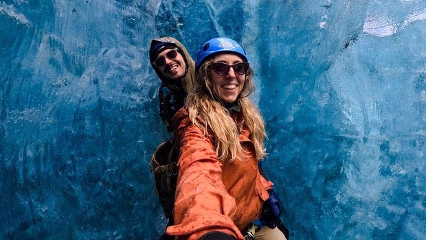 两名头戴头盔、身穿户外装备的人在明亮的蓝色冰洞内用 GoPro 自拍。他们面带微笑，周围环绕着纹理丰富的冰壁。 