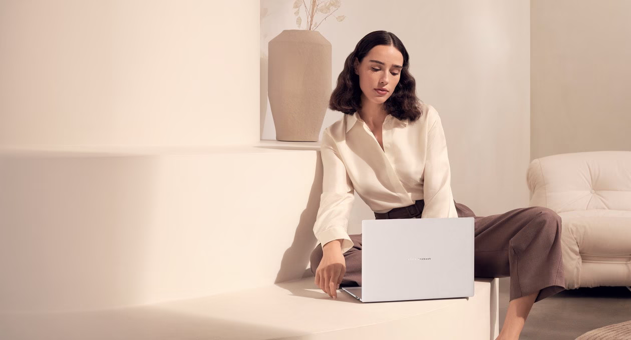 A person sits in a serene, minimalist space with a white laptop, surrounded by soft neutral tones and elegant decor. 