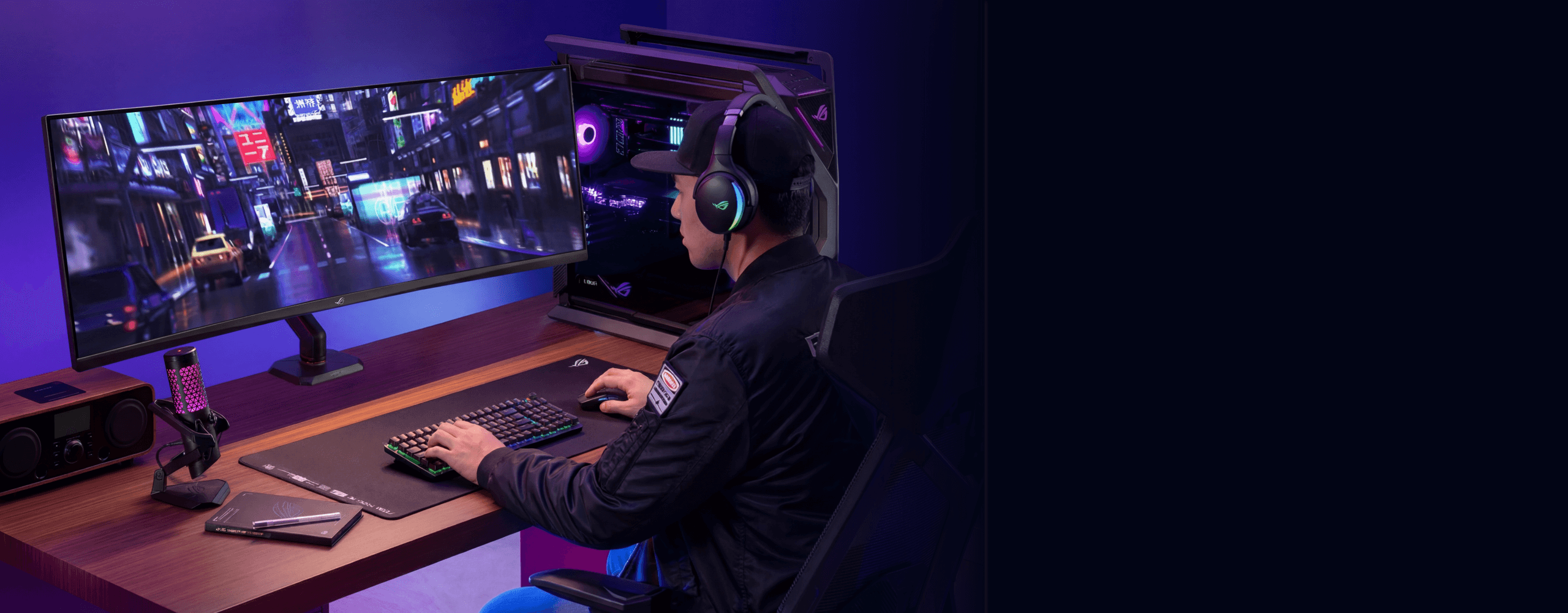 一位戴着帽子和游戏耳机的人正全神贯注地玩着视频游戏，游戏画面显示在安装于ROG AAS01R人体工学支架上的49英寸显示器上。该配置包含一台带RGB灯效的台式电脑，搭配机械键盘、鼠标、麦克风和音箱，整体置于木质书桌上。