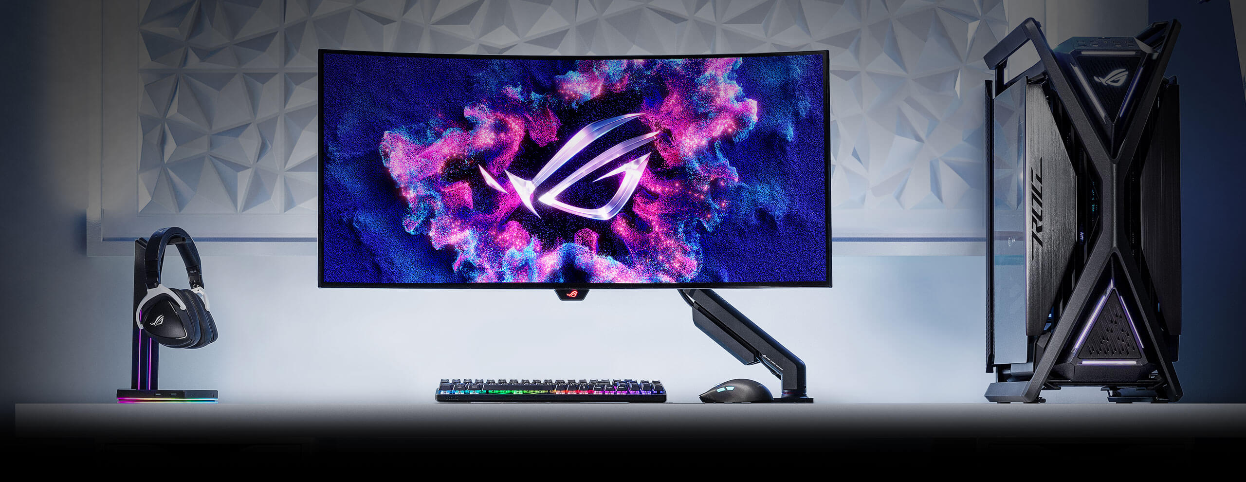 一套游戏设备，包含安装在ROG人体工学显示器支架上的ROG显示器、键盘与鼠标、电脑以及耳机。