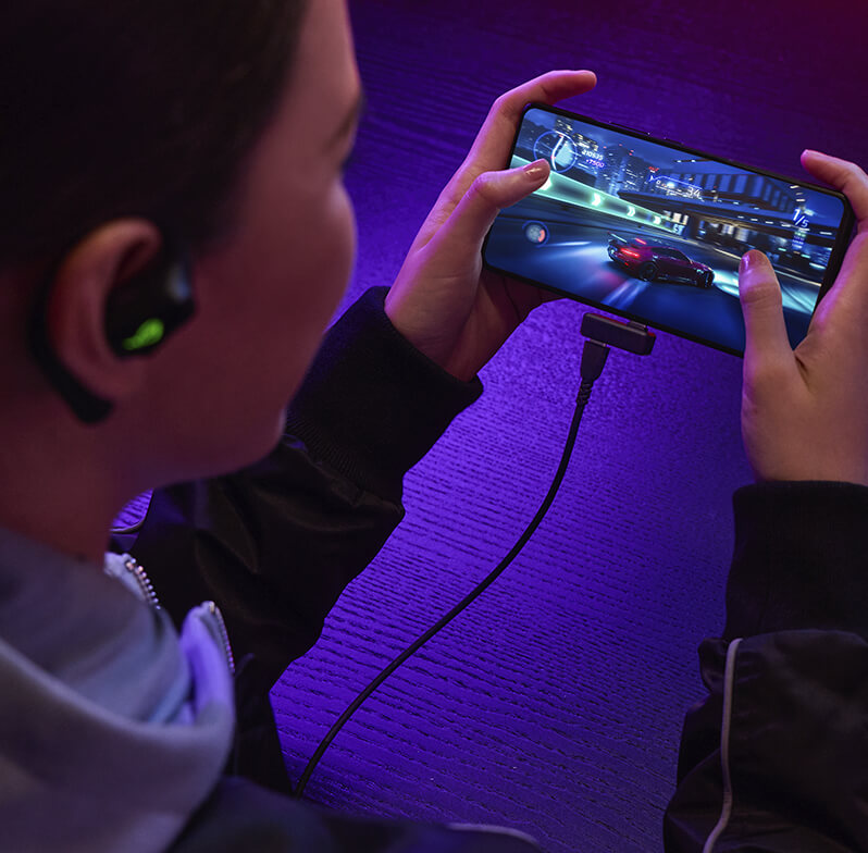 女性在智能型手机上玩游戏，同时通过 USB-C 旁路充电为 ROG 降临OWS 充电