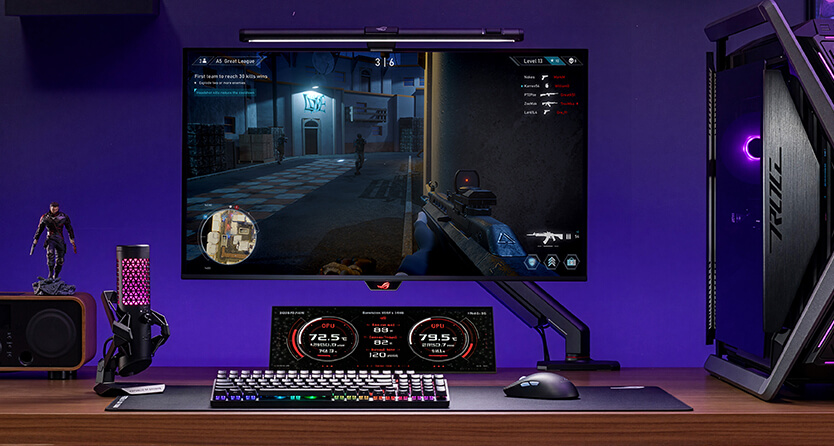 一套 ROG 游戏设备,显示器上显示着 FPS 游戏画面;该设备包括 RGB 键盘、麦克风、扬声器和 PC,在黑暗的房间里,PC 周围环绕着紫色的环境灯光。