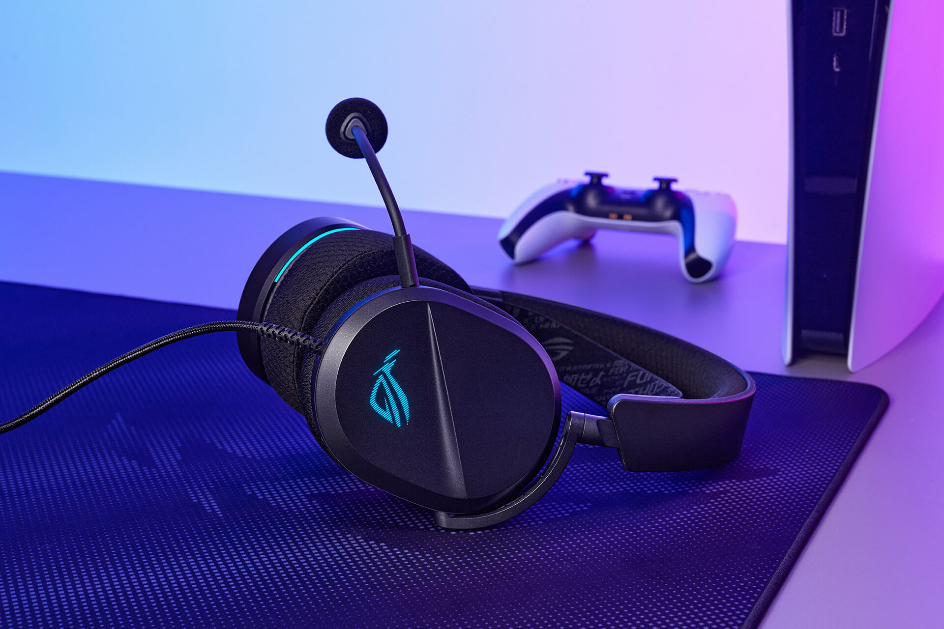 ROG 破风 标准版gaming headset placed on a desk next to a Playstation gaming console and its wireless controller.