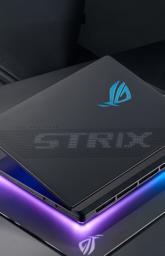 ROG 枪神笔记本电脑发光 ROG 标志与 STRIX 文字特写，下方映衬着紫色光影。
