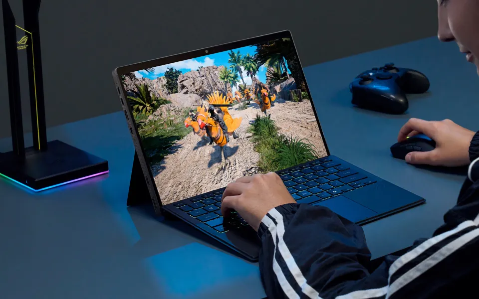 A person sitting at a desk with a laptop, coffee, mouse, and headset, playing a game on their machine 