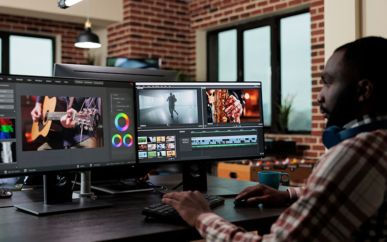 一名非洲男子在办公桌前使用两台显示器编辑视频。