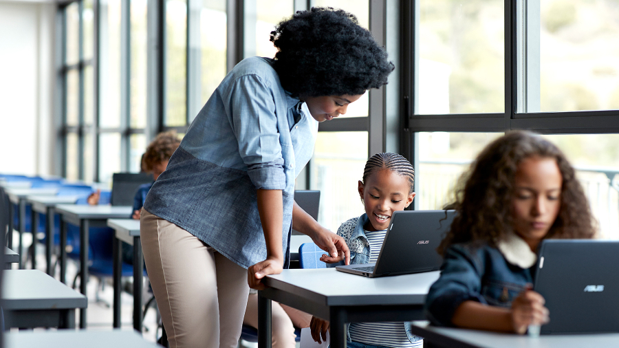 孩子们在教室使用自己的 ASUS BR1100 笔记本电脑，一位老师正在教一个女同学并同时看着笔记本电脑屏幕。