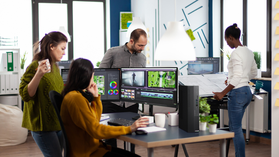 四名负责创意制作的工作人员在办公室工作，其中两人正讨论影片编辑，桌上放着 ASUS ExpertCenter 商用台式电脑和 ProArt 屏幕。