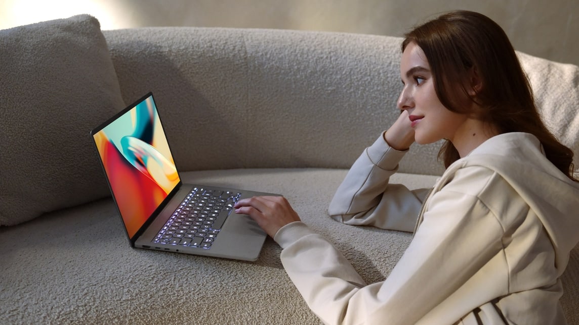 An image showcases a woman watching a colorful video on a gray Zenbook A14.