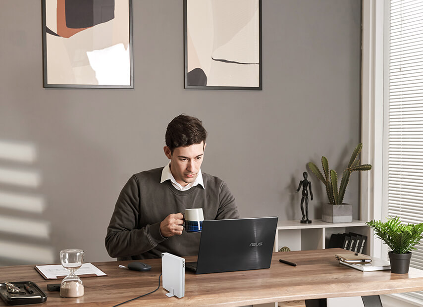 A man is at home using a laptop with the RT-AX57 Go router placed on the desk.