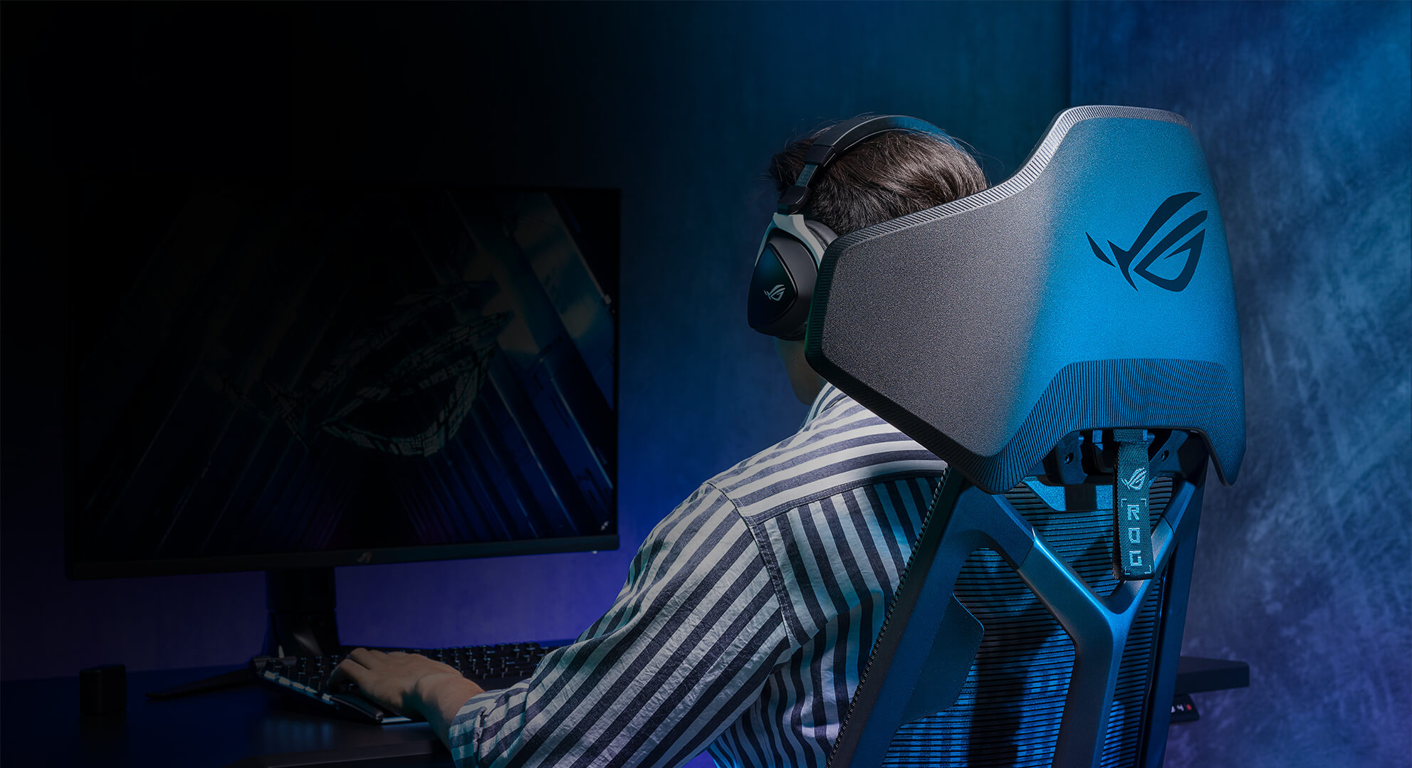 一名男子坐在 ROG Destrier Ergo 电竞椅上玩 PC 游戏的斜后方视角画面