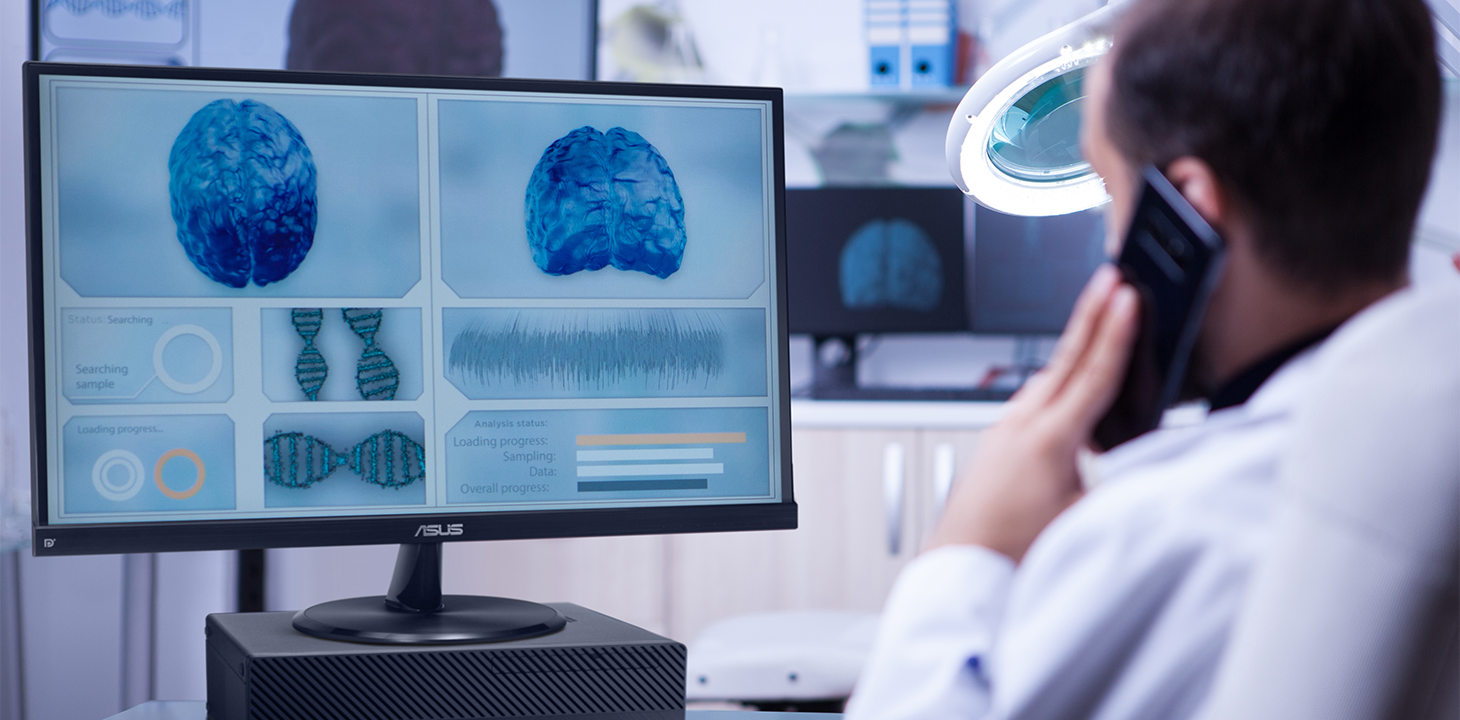 一名健康照护人员正在使用 ASUS ExpertCenter 桌面计算机和屏幕查看脑部影像和一些分析数据，同时使用手机通话。