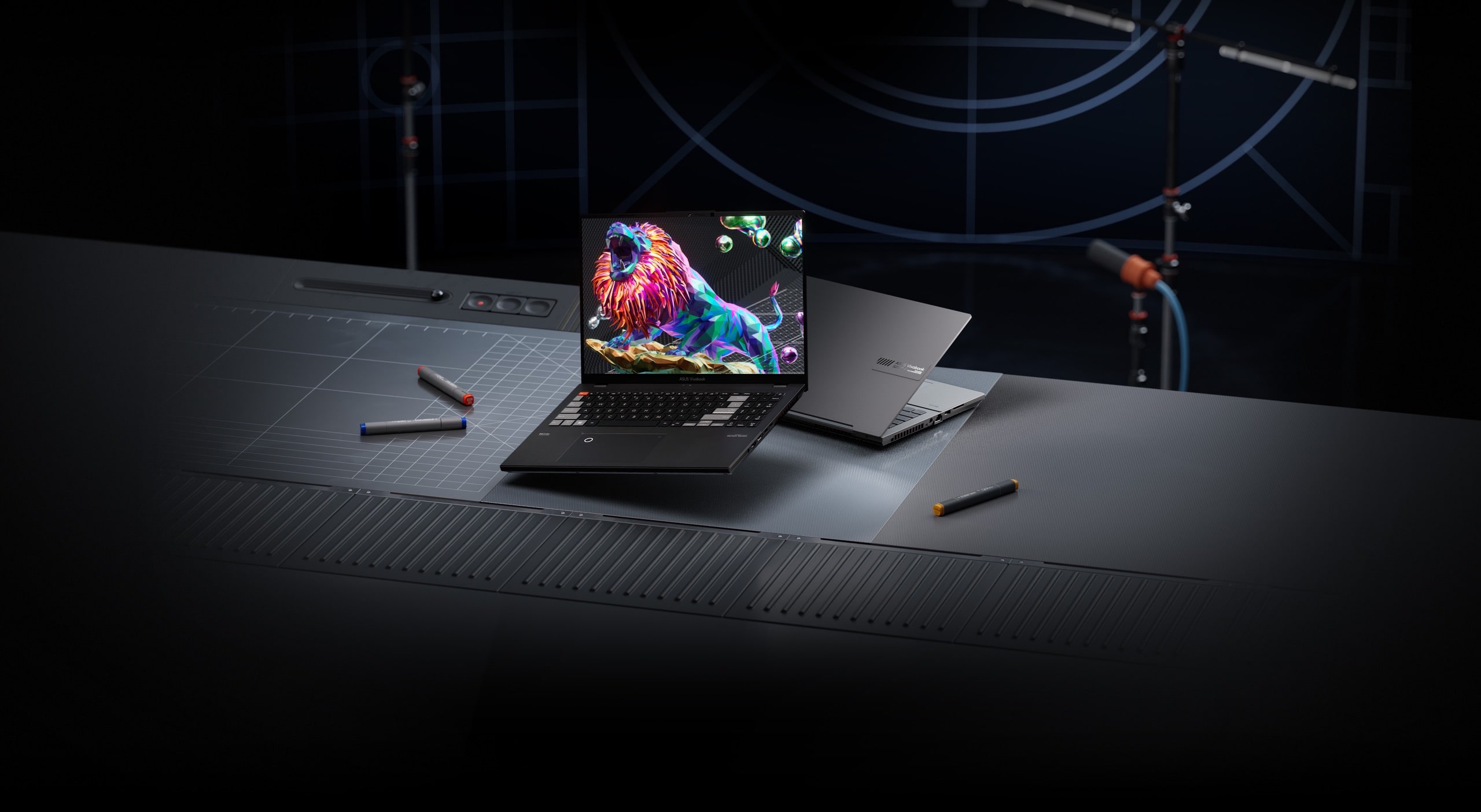 A black and silver 华硕无畏Pro16 2023 旗舰版 (K6604) model is shown on a recording studio desk, with the black laptop in-screen showing a lion roaring.