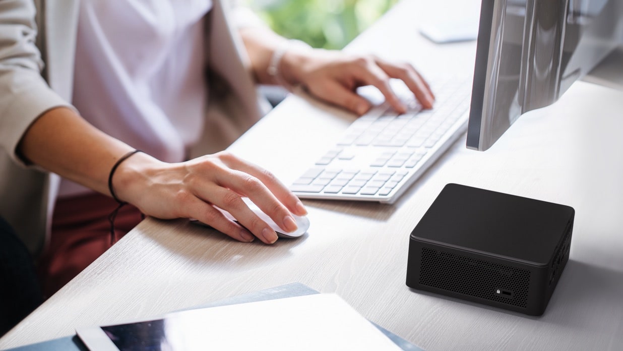 a person without showing face, Holding the mouse in one hand, and putting the other hand on the keyboard, facing the screen, A NUC 11 Performance mini PC on the table.